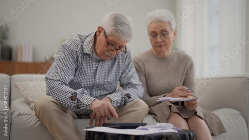Worried senior retired couple checking calculating bills sitting on couch at home. Do paperwork discuss unpaid debt taxes, stressed family. Financial difficulties, money problem in elderly age concept photo