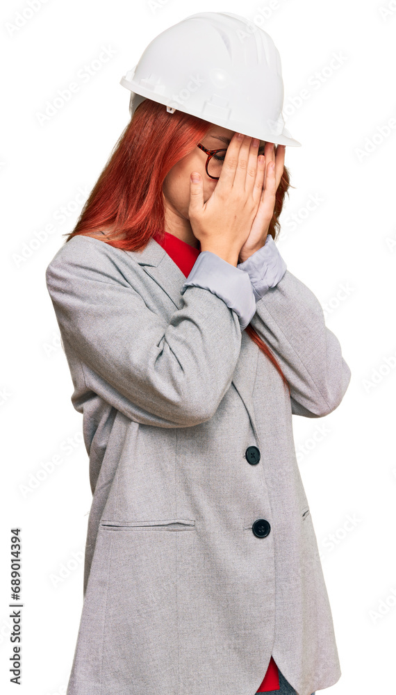 Young redhead woman wearing architect hardhat with sad expression covering face with hands while crying. depression concept. Young redhead woman wearing architect hardhat with sad expression covering face with hands while crying. depression concept.