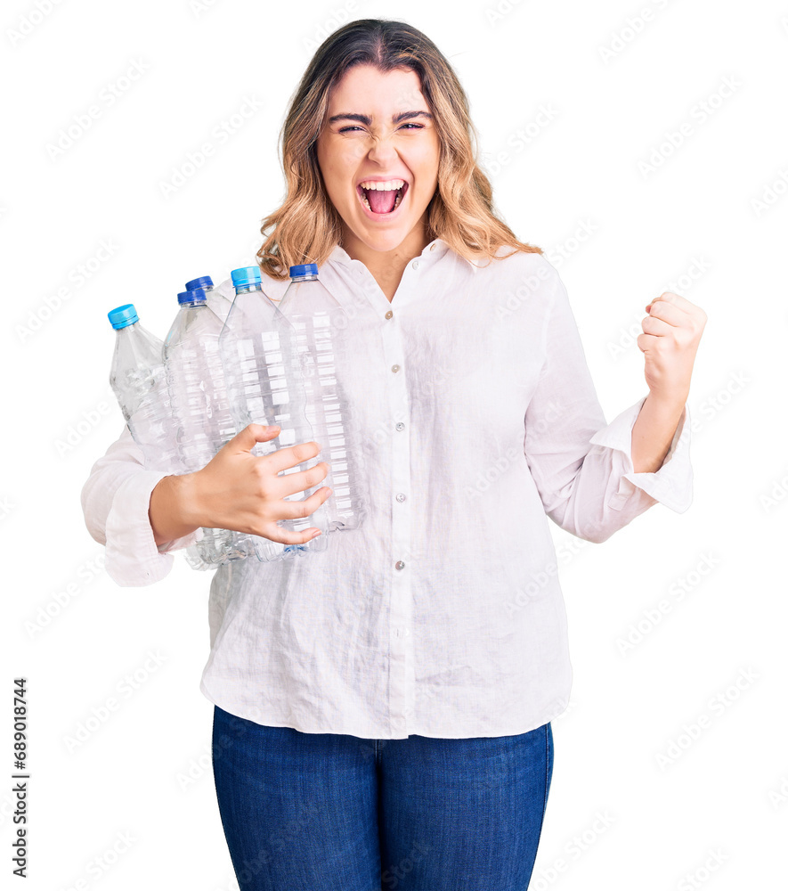 Young caucasian woman holding recycling plastic bottles screaming proud, celebrating victory and success very excited with raised arms Young caucasian woman holding recycling plastic bottles screaming proud, celebrating victory and success very excited with raised arms