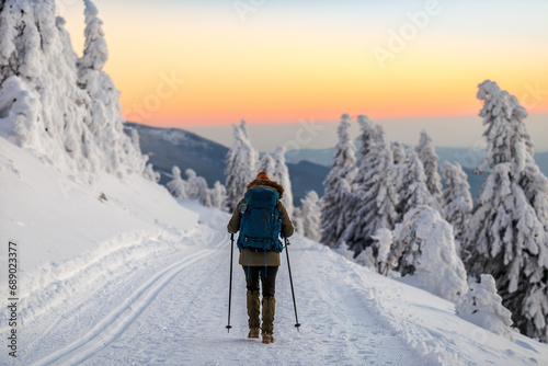 Woman hiking in snow on trekking trail at winter mountains during sunset. Sports and outdoors seasonal activity