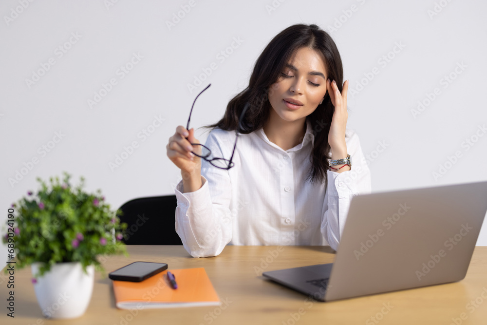 Attractive young businesswoman working on laptop and smiling while sitting at her desk in bright modern office Attractive young businesswoman working on laptop and smiling while sitting at her desk in bright modern office