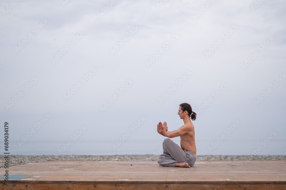 Caucasian man with naked torso practicing wushu on the seashore. 