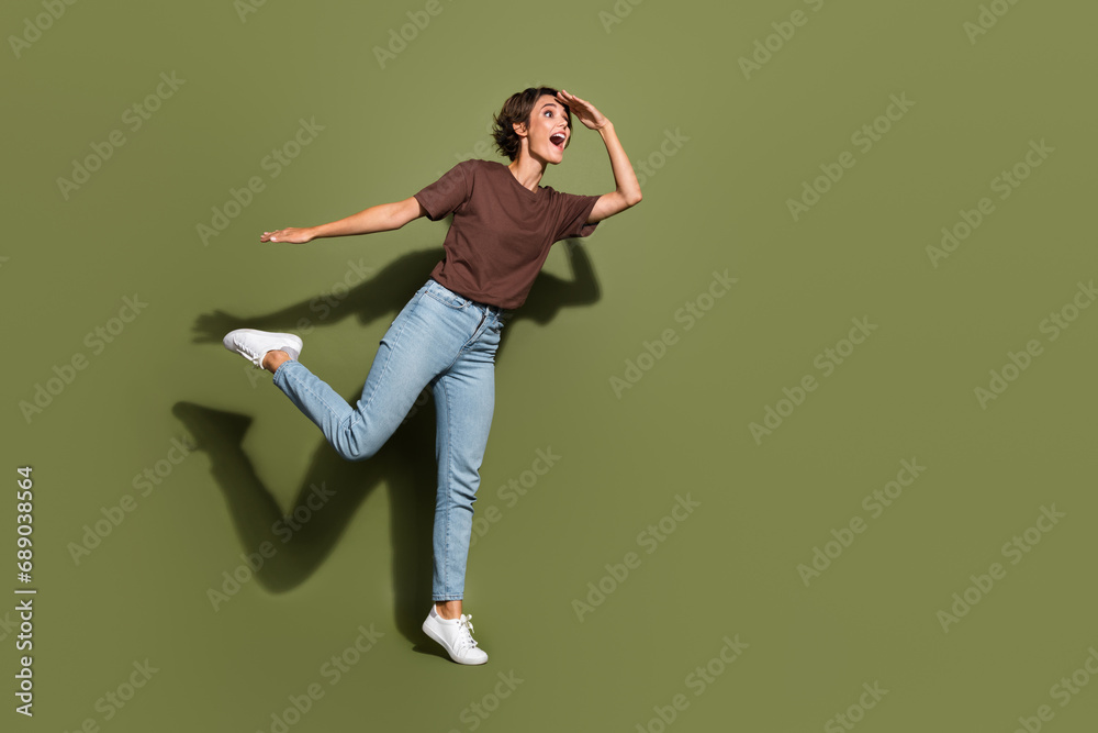 Full size photo of funny woman dressed brown t-shirt jeans hold arm on forehead look far at empty space isolated on khaki color background