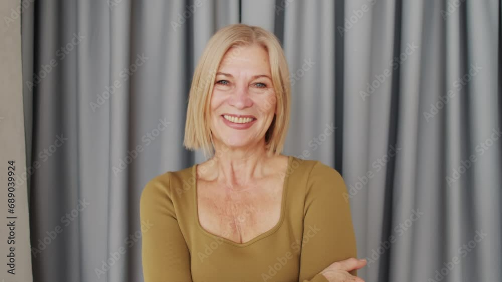 Horizontal medium close-up portrait of beautiful mature woman with blond bob cut hair wearing khaki green clothes smiling at camera