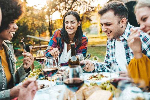 Happy friends having bbq dinner party in garden restaurant - Multiracial young people eating grill meat and drinking red wine in backyard - Food life style concept with guys and girls sitting outdoors photo