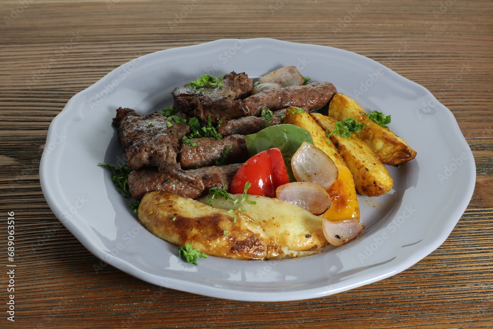 Mix kofta kabab and lamb chop with potato veggies, tomato and onion served in dish isolated on table side view of arabic food