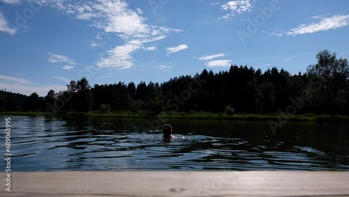 Young woman swimming in a natural lake located in the Bavarian Forest on a sunny day