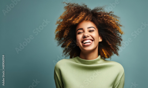 Joyful Black woman with a big smile and natural curly hair in a casual green sweater on a grey background