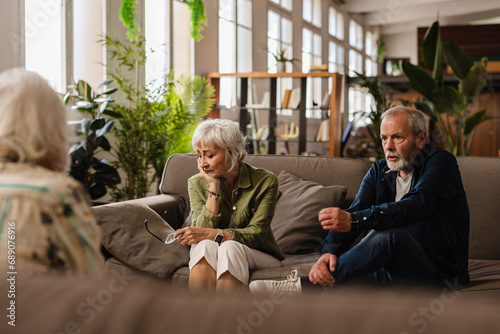 An unhappy elderly couple arguing, helped by psychologist therapy. Frustrated wife and husband discussing relationship problems with their therapist - mental health concept photo