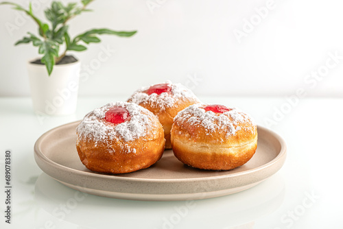 sweet freshly baked donuts with strawberry filling on ceramic plate on white glass surface close up