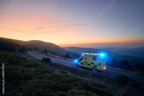 Ambulance car of emergency medical service mountain road against sunrise. Moody sky with copy space. Themes rescue, urgency and health care.. © Chalabala