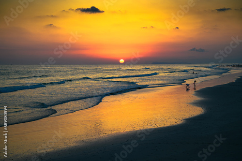 Sunset above Arabian Sea and a beach in Salalah, Oman, against a clear summer sky with silhouettes of people