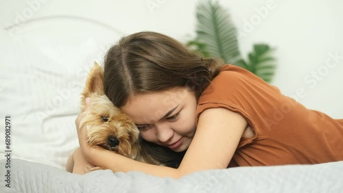 The girl is lying on the bed at home and hugging her Yorkshire Terrier dog.