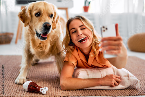 Fun together. A happy woman is taking a selfie with her cheerful pet, who has a funny expression on his face, and they are lying on the living room floor and making funny faces.Emotional connection. photo