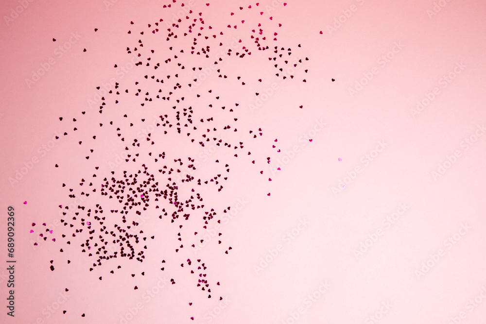 Fototapeta premium Greeting background with empty space. Violet sparkle sequins, glitter in heart shape on a gentle pink background. Top view