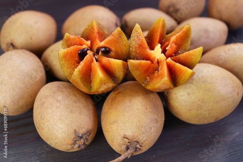 Beautifully Cut Sapodilla Fruit and Heap of Whole Fruits on Black Wooden Background photo