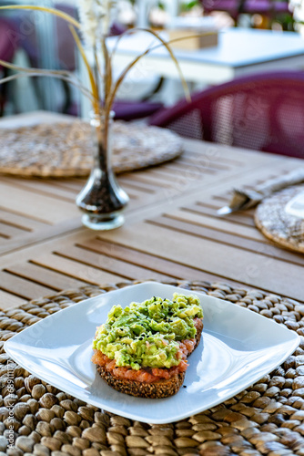 a portrait image of a slice brown seeded slice of toast topped with smashed avocado at a mediterranean restaurant  photo