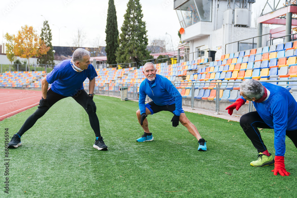 Elderly athletic men performing warm-up stretches on a stadium track, showcasing active senior lifestyle Elderly athletic men performing warm-up stretches on a stadium track, showcasing active senior lifestyle