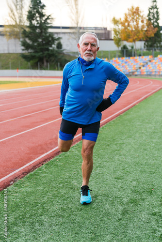 Mature Caucasian athlete in blue takes a break on running track, embodying active senior lifestyle