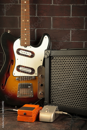 Vintage electric guitar, guitar amplifier and effects pedals for the guitarist on a dark brick background.
