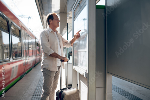 Passenger searching train in timetable on train station in city.