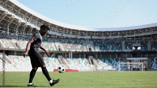 African American man playing football on the stadium field. A man runs with a soccer ball across the field. © Katsiaryna