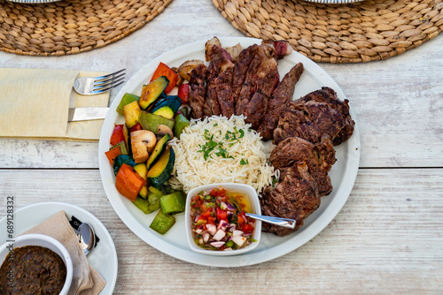 a view over a plate of grilled meat served with rice and mixed vegetables at a restaurant.