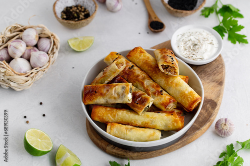 Turkish Cigara Börek (Sigara böreği) or Cigarette Pastry with Spinach and Feta Cheese with yogurt dip. Finger food. Spring rolls. Top view photo