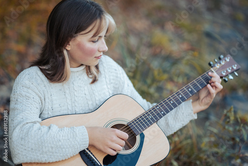 Girl playing the guitar. Portrait of a young girl playing the guitar outdoors, mastering her skills