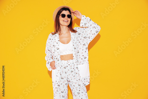 Young beautiful smiling female in trendy summer costume clothes. Carefree woman posing near yellow wall in studio. Positive model having fun indoors. Cheerful and happy. In hat and sunglasses © halayalex