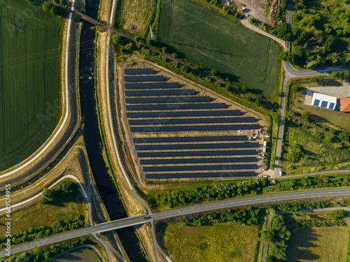 Top down drone shot of solar panels between fields, river and streets