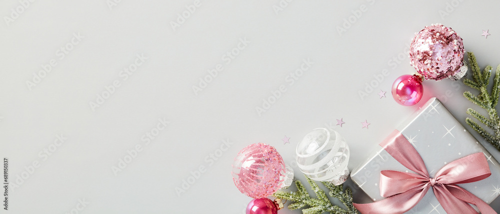 Christmas banner. Chic gift box with pink ribbon bow, glitter balls, decorations, fir branches on grey background. Top view with copy space. Flat lay.