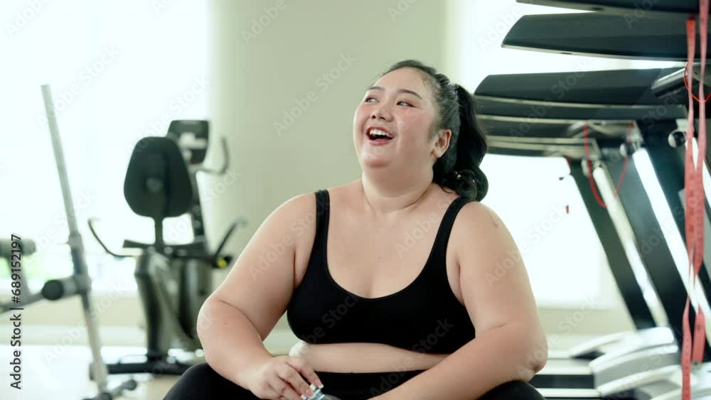 Happy Chubby woman sitting and resting after exercising in gym. Cute Asian overweight woman exercise try to lose weight Sit down and drink some water to relieve tiredness after running on treadmill. Happy Chubby woman sitting and resting after exercising in gym. Cute Asian overweight woman exercise try to lose weight Sit down and drink some water to relieve tiredness after running on treadmill.