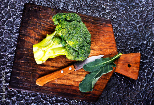 fresh green broccoli on wooden cutting board with knife. Broccoli cabbage leaves. dark background.
