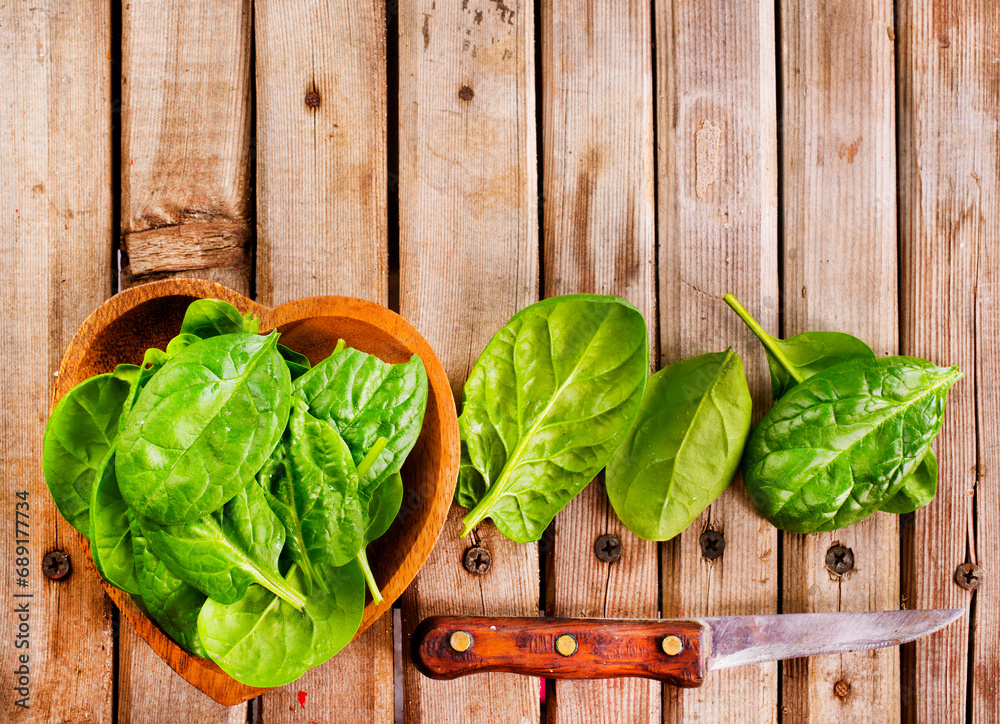 Fototapeta premium Fresh spinach leaves in bowl on rustic wooden table. Top view.