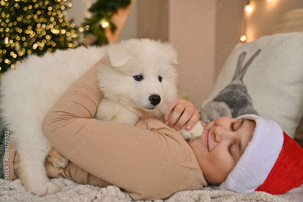 Christmas at home. Children and Samoyed puppies under the Christmas tree. Small children in a Santa hat hug a pet and open Christmas presents. Children are playing with an animal. Christmas at home. Children and Samoyed puppies under the Christmas tree. Small children in a Santa hat hug a pet and open Christmas presents. Children are playing with an animal.