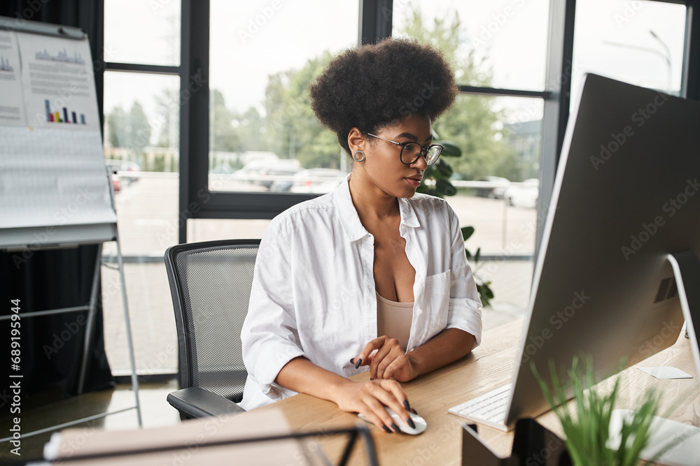 concentrated african american businesswoman in eyeglasses working on computer in contemporary office