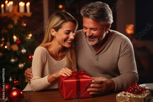 Smiling Middle Aged European Couple Holds Christmas Gift in Beautifully Decorated Living Room. © pkproject