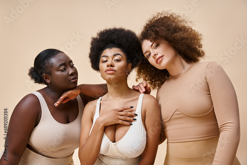 confident and charming multiethnic women in underwear on grey backdrop, natural plus size beauty