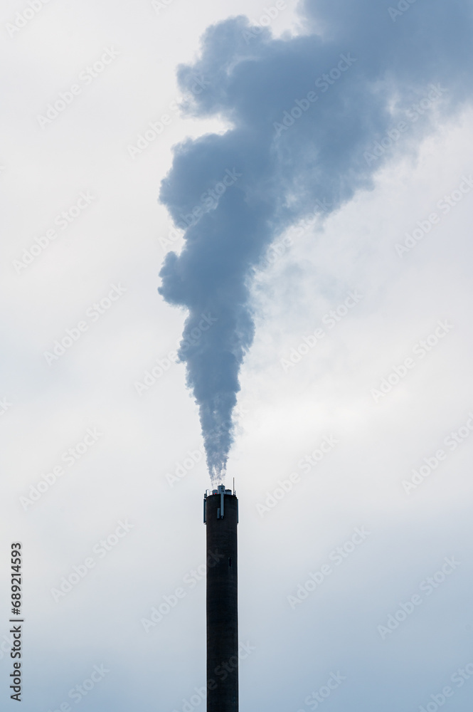 High chimney with pillar of smoke against grey sky