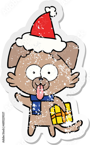 hand drawn distressed sticker cartoon of a dog with christmas present wearing santa hat