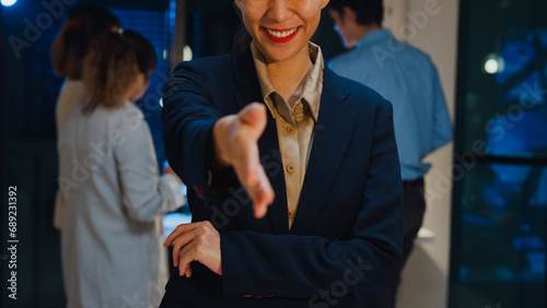 Portrait of successful executive businesswoman smart casual wear shaking hands and looking at camera and smiling happy in modern night office workplace. Partner cooperation, coworker teamwork concept. photo