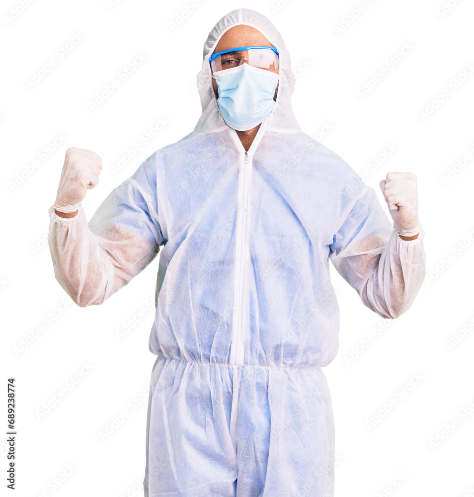Young hispanic man wearing doctor protection coronavirus uniform and medical mask celebrating surprised and amazed for success with arms raised and open eyes. winner concept.