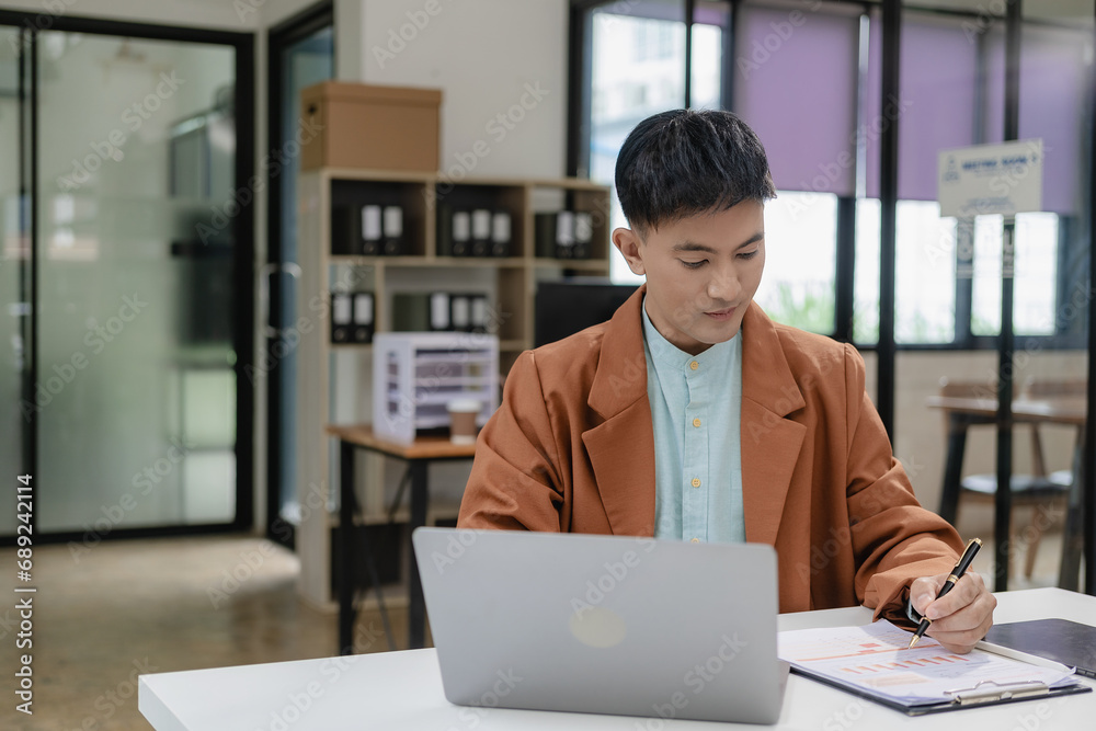 Fototapeta premium Businessman, manager, CEO, handsome Asian man, middle aged man sitting in office, working on paperwork, checking and reading documents, contracts and accounting reports with laptop.
