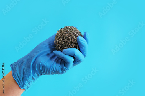 Stainless steel kitchen brush. Barbecue cleaning tools. A hand in a latex blue glove holds a stainless steel ball brush. Dishwashing brush, kitchen tool, blue background