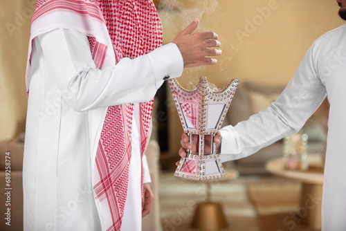фотографія An Arab man holds a censer for his guesr perfumes him with it