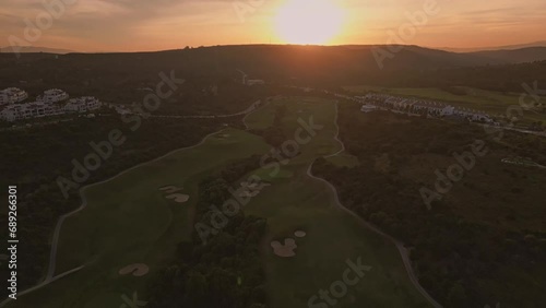 Establishing aerial panoramic view of a green golf course. Drone flying over golf club on a beautiful sunset photo