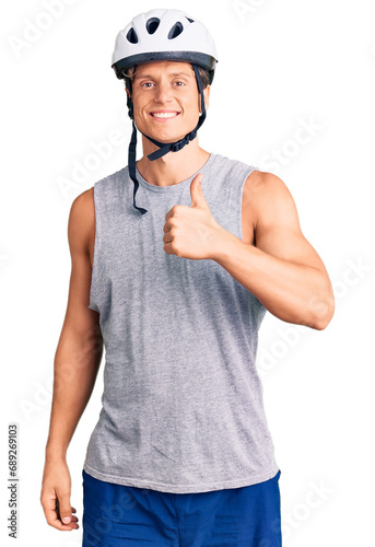 Young handsome man wearing bike helmet doing happy thumbs up gesture with hand. approving expression looking at the camera showing success. © Krakenimages.com