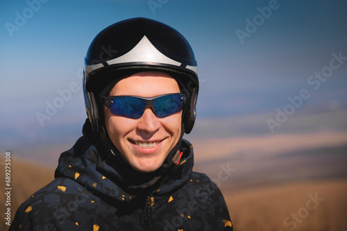 Portrait of a smiling young man with a parachute in a field. A guy paraglider in sportswear and a helmet is preparing for a flight or after landing outdoors © yanik88