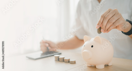 a man hand putting money coin into piggy for saving money wealth and financial concept. Businessman is calculating income and return on investment.